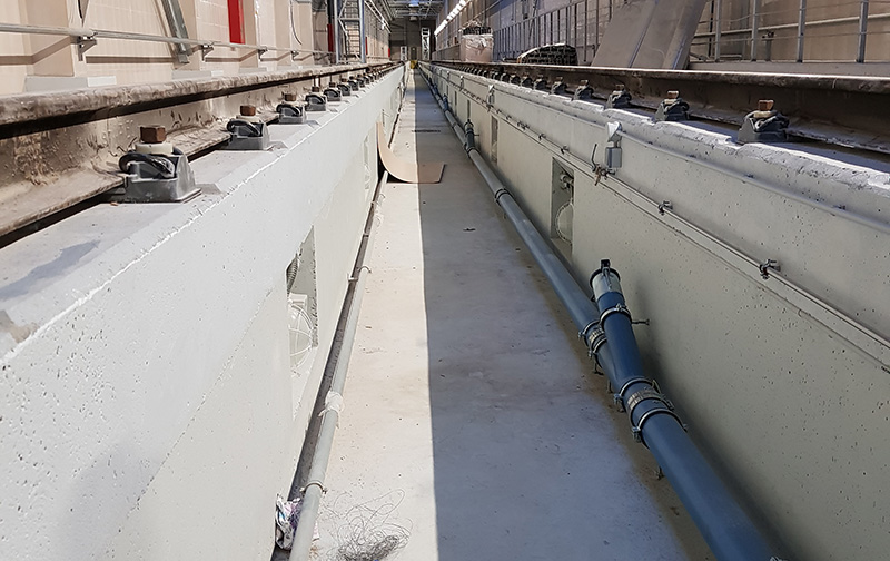 Long concrete trench housing a DISAB pre-separator pipeline system, designed for connection to an industrial vacuum unit, with mounted hoses and metal fittings running the length of the structure for efficient material transport and separation.