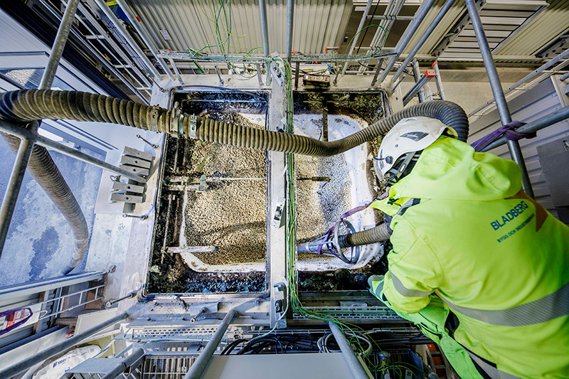 Worker in high-visibility gear operating DISAB hoses on a metal platform, managing material collection in a complex, elevated industrial environment with multiple suction lines.