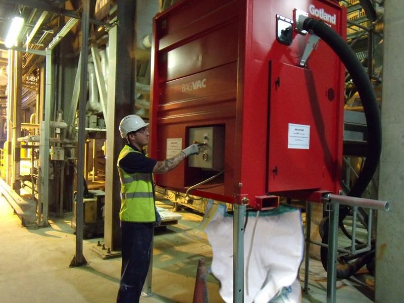 Factory worker operating a DISAB BagVAC unit installed indoors with a connected suction hose, demonstrating hands-on usage for dust and material extraction in industrial environments.