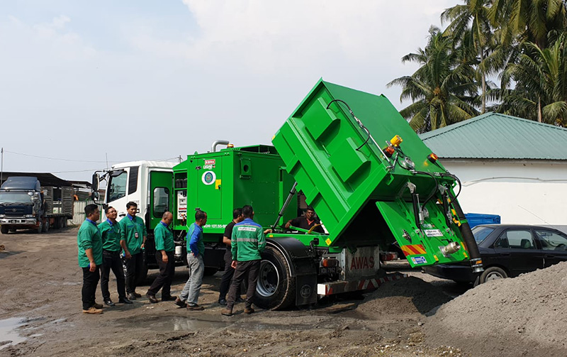 Green DISAB TrailerVAC SDR-10T vacuum truck parked on an industrial site with a group of workers standing nearby, showing the unit's mobility and suitability for waste collection and heavy-duty cleaning in large facilities.
