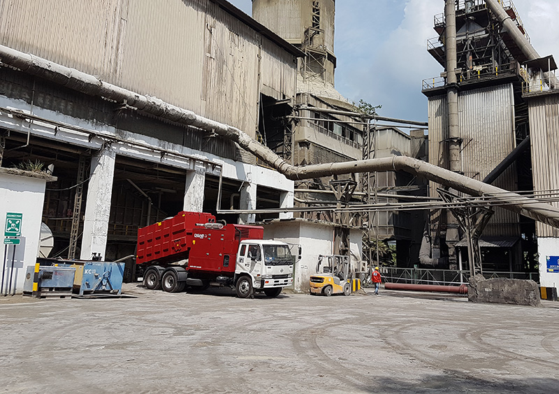 Red DISAB TrailerVAC industrial vacuum truck parked outside a large processing facility, showcasing its mobility and ability to handle dust and material extraction in complex industrial environments.