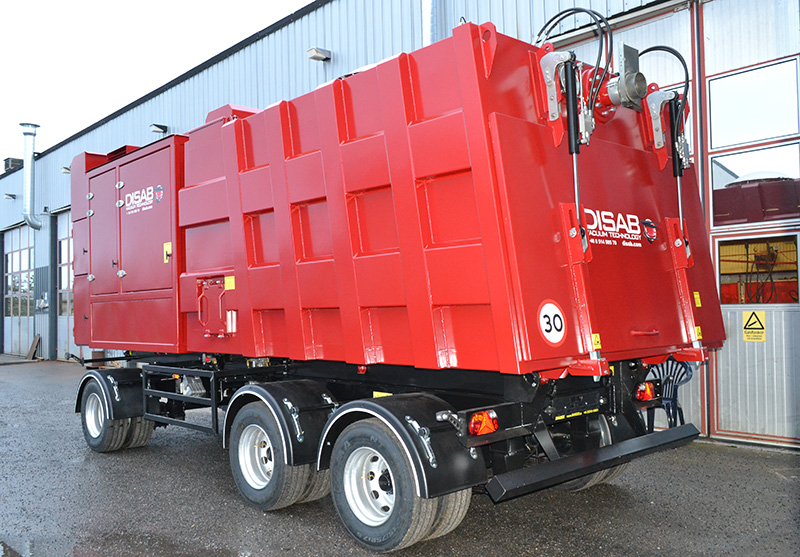 Red DISAB TrailerVAC SDT-20T vacuum trailer parked outside an industrial facility, featuring a multi-axle chassis and enclosed dust container, ready for heavy-duty cleaning and material transport tasks.