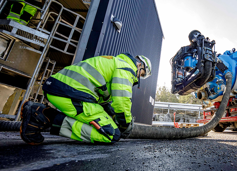 Worker in reflective safety gear connecting or managing a large industrial suction hose attached to a DISAB Futurion™ Q20 unit, demonstrating safe material extraction procedures at an outdoor facility.